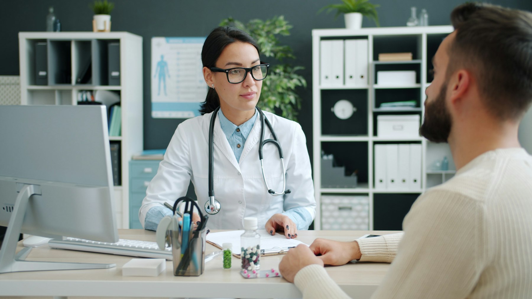 A physician in a white coat talking with a patient across a desk
